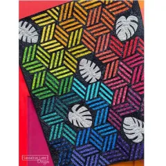 Nahaufnahme des fertigen Quilts mit Streifen-Hexagonen in Regenbogenfarben von Gelb bis Lila und hellgrauen Monstera-Blatt-Applikationen auf schwarzem Grund.